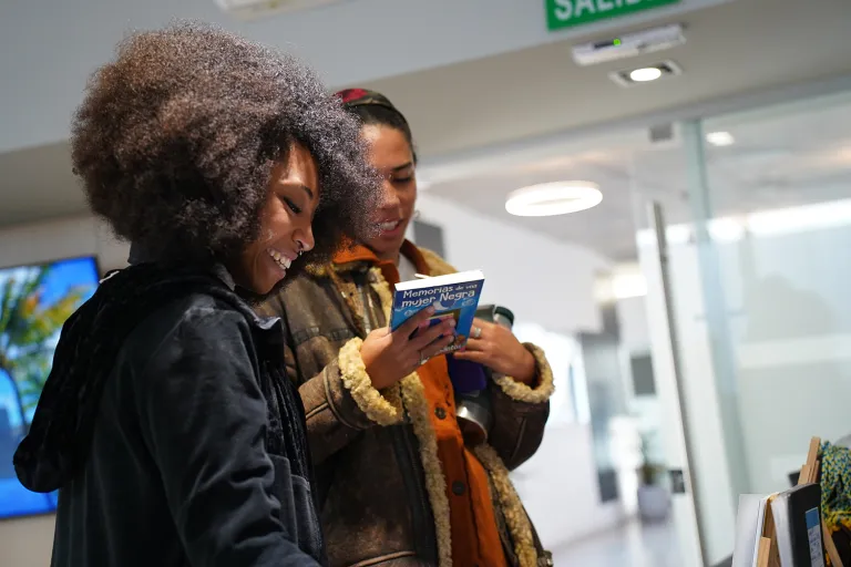 Dos personas consultan el libro "Memorias de una mujer Afro" durante una actividad en un espacio universitario.